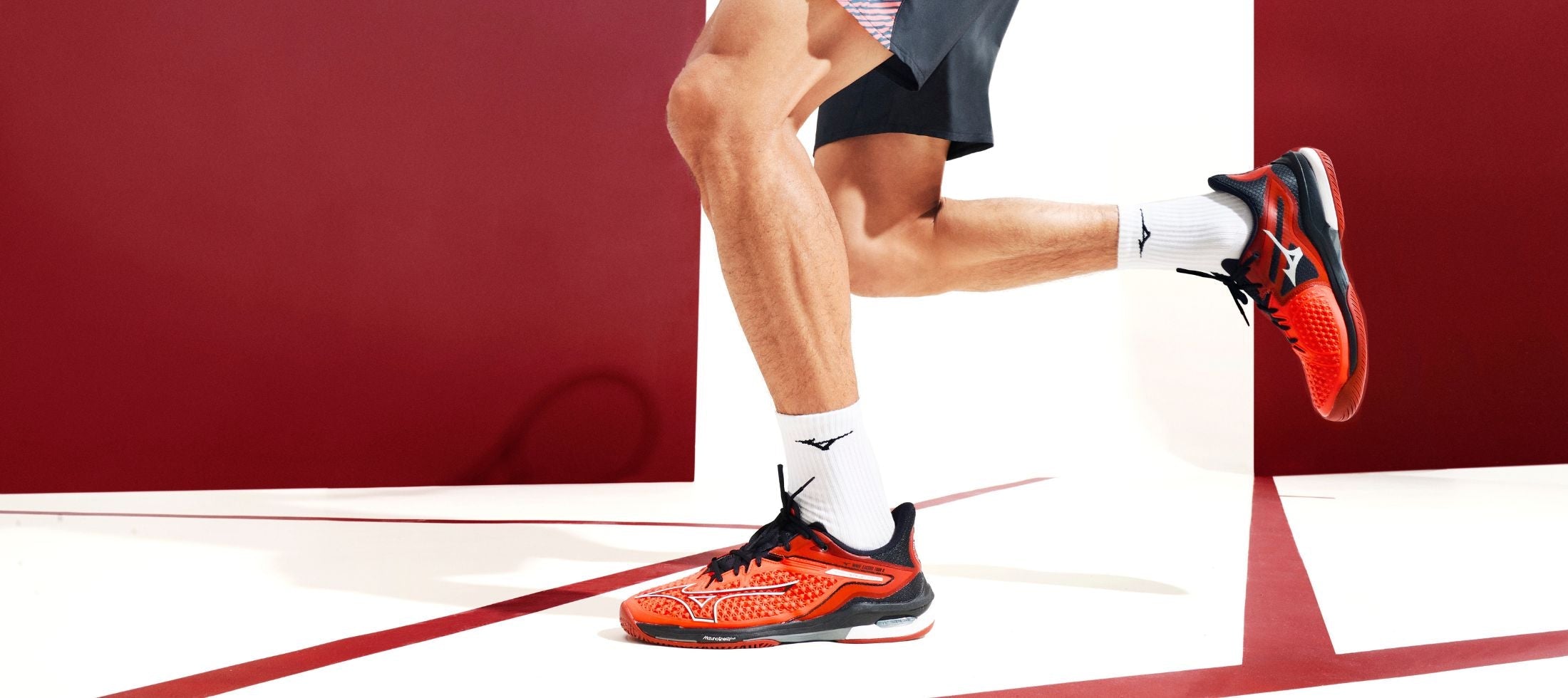 A Male playing tennis and wearing red tennis shoes