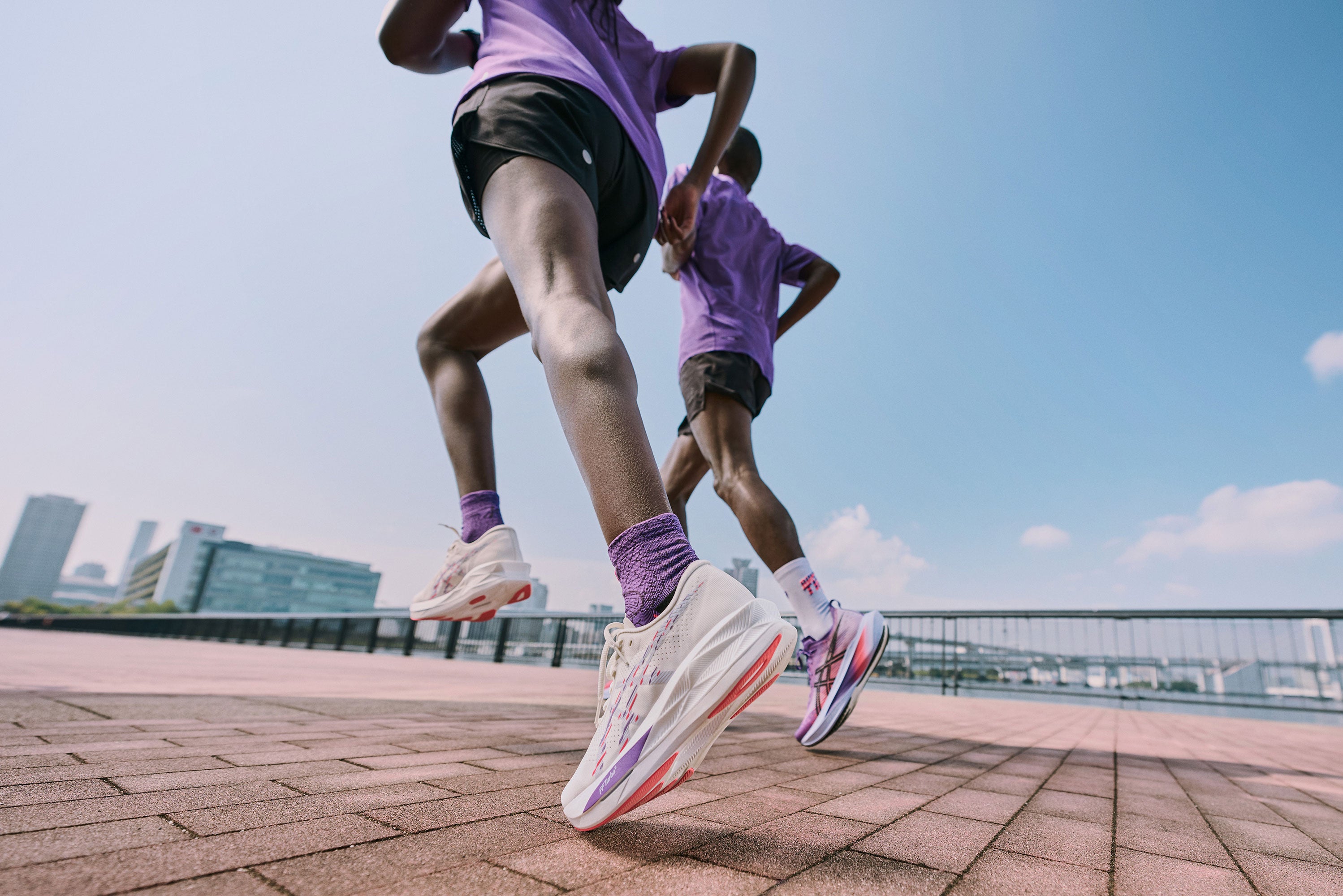 Two runners in purple shirts and white running shoes on a city street.